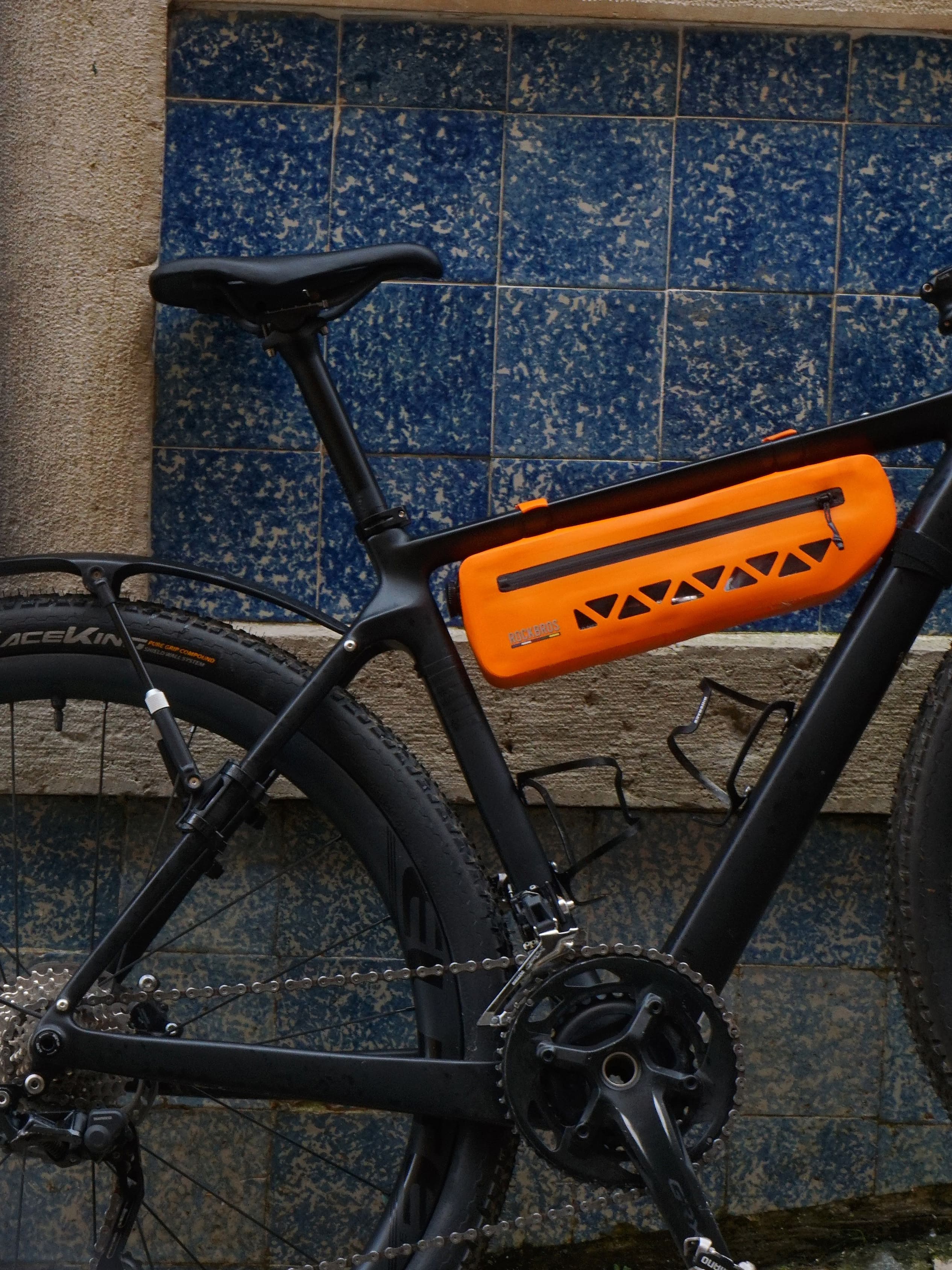 Black bicycle with an orange frame bag against a blue tiled wall.